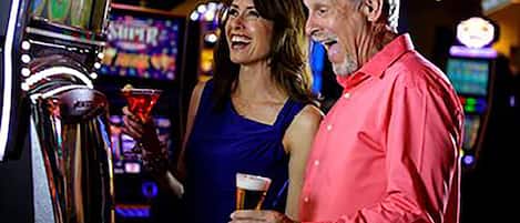 A man and a woman standing in front of a slot machine, holding drinks.