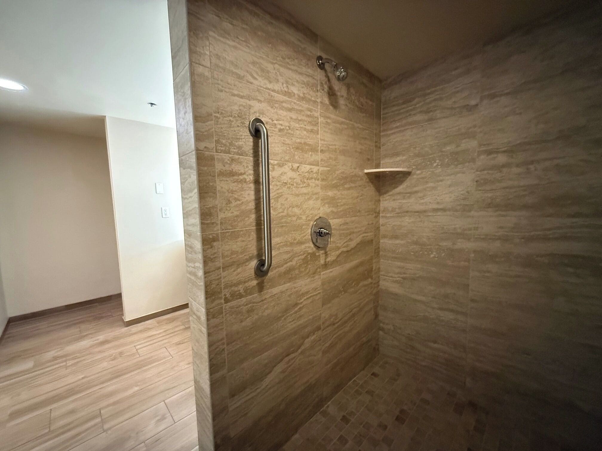 Un baño con zona de ducha, barra de apoyo y lavamanos en esquina.