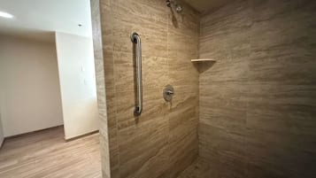 A bathroom with a shower area, a handrail, and a corner sink.