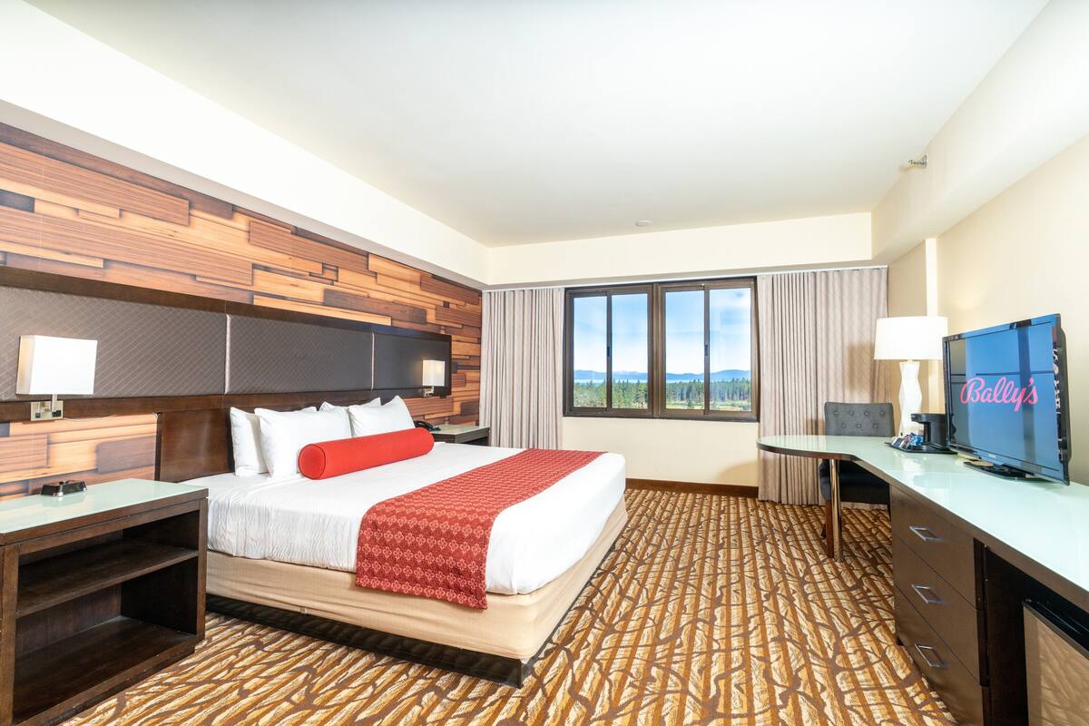 Ein Hotelzimmer mit einem großen Bett, einem Schreibtisch mit Fernseher und einem Fenster mit Blick ins Freie.
