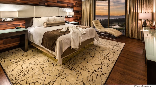 Een moderne hotelkamer met een groot bed, een chaise longue, uitzicht op de stad en een houten accentmuur.