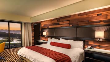 A hotel room with a large bed, a view of a landscape through the window, and a wooden headboard.