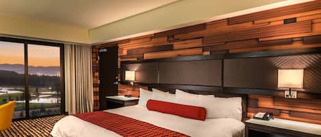 Une chambre d’hôtel avec un grand lit, une vue sur le paysage par la fenêtre et une tête de lit en bois.