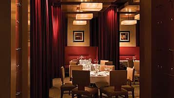 A dining area with a table set for four, surrounded by chairs, in a room with red curtains and framed pictures on the walls.