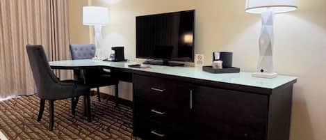 A hotel room with a desk, chair, television, and two lamps.