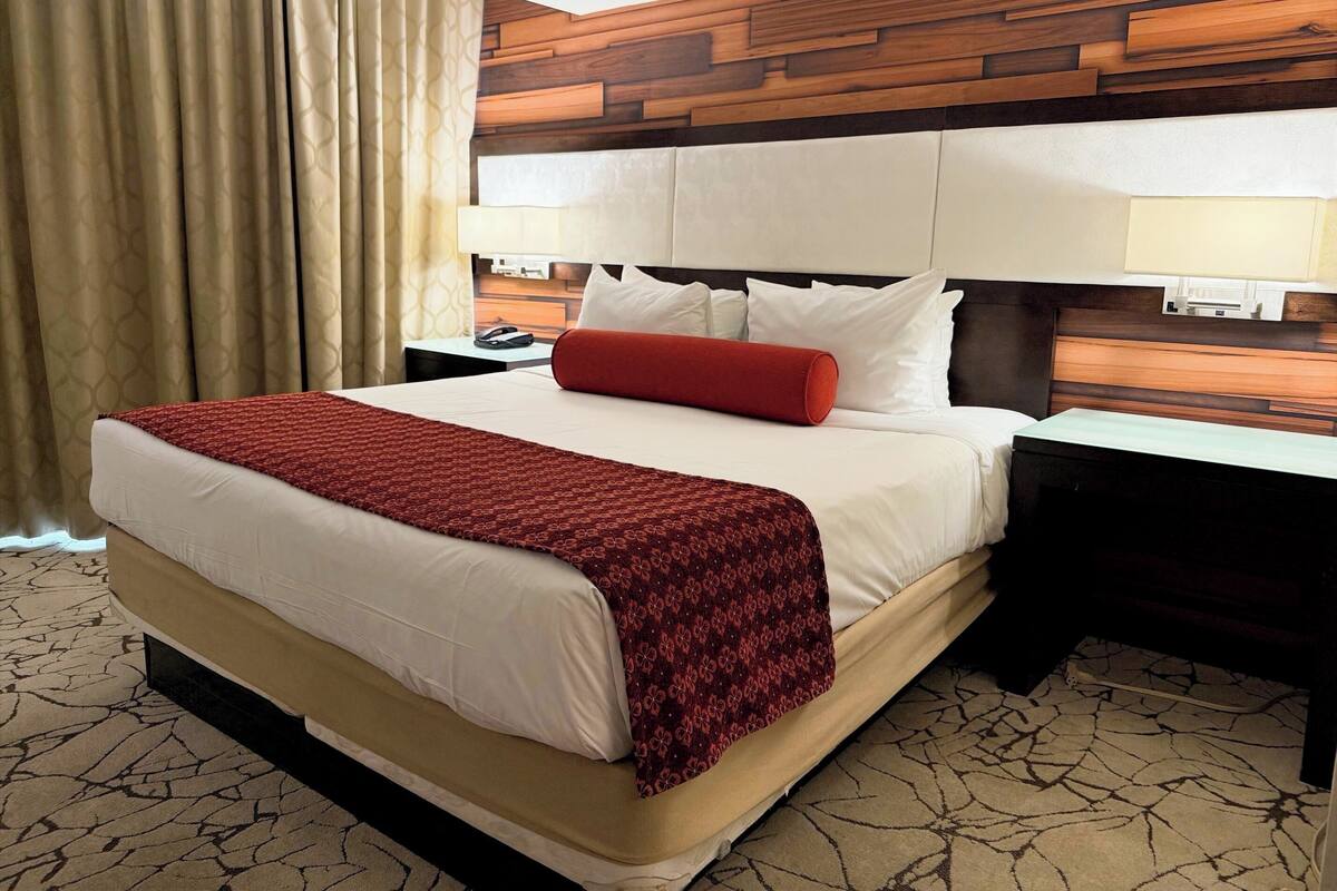 Ein Hotelzimmer mit einem großen Bett, einem Holz-Kopfteil, zwei Nachttischen und einem gemusterten Teppich.