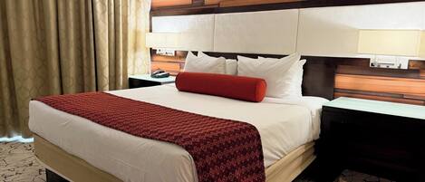 Una habitación de hotel con una cama grande, un cabecero de madera, dos mesitas de noche y una alfombra estampada.