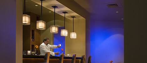 Un restaurante con sillas y mesas de madera, una zona de bar e iluminación colgante.