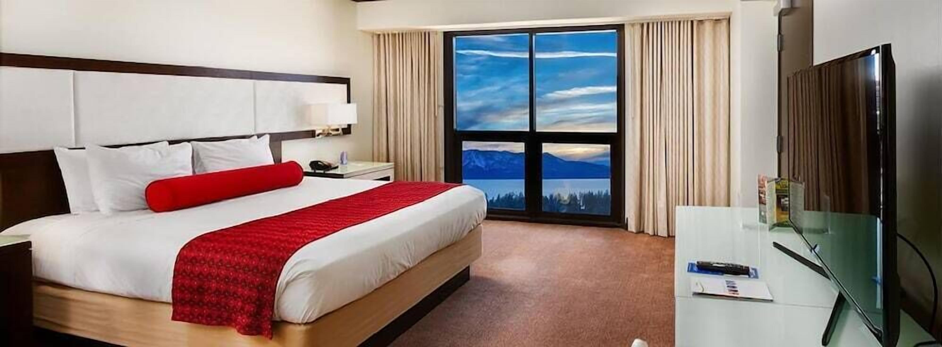 Een hotelkamer met een bed, een bureau, een televisie en een groot raam met uitzicht op de bergen.