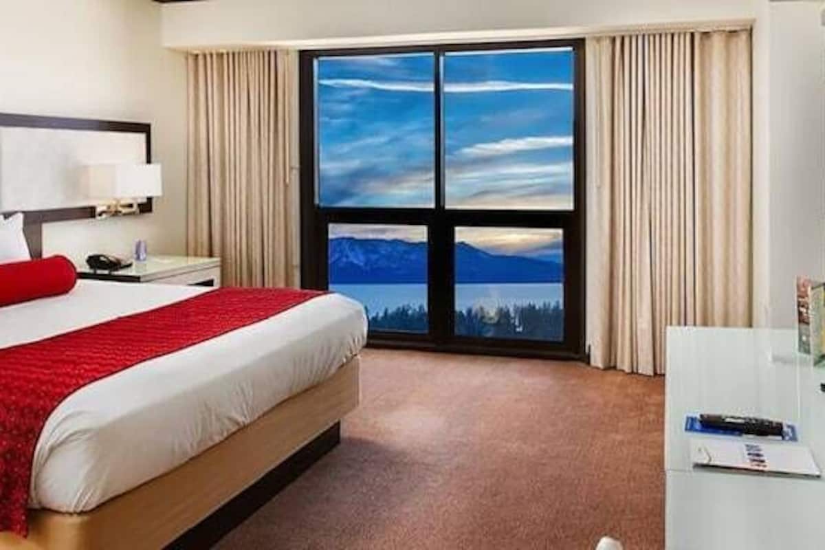 A hotel room with a bed, a desk, a TV, and a large window with a mountain view.