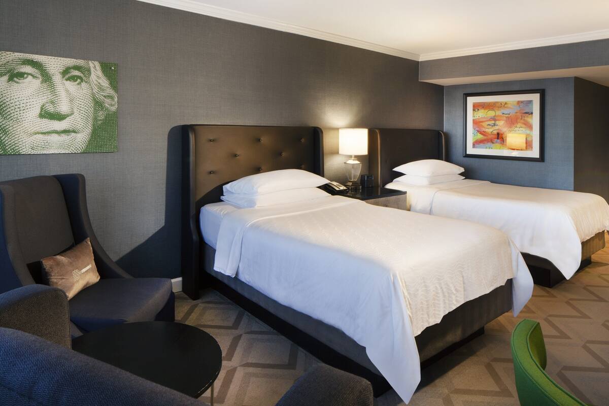 A hotel room with two beds, a sofa, a small table, and artwork on the walls.