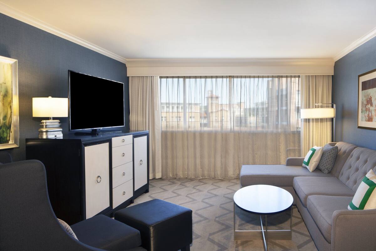A modern hotel room with a flat-screen TV, a sofa, a coffee table, and a desk with drawers.