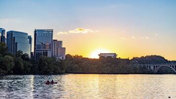 A city skyline with modern buildings, a bridge, and a sunset over a body of water.