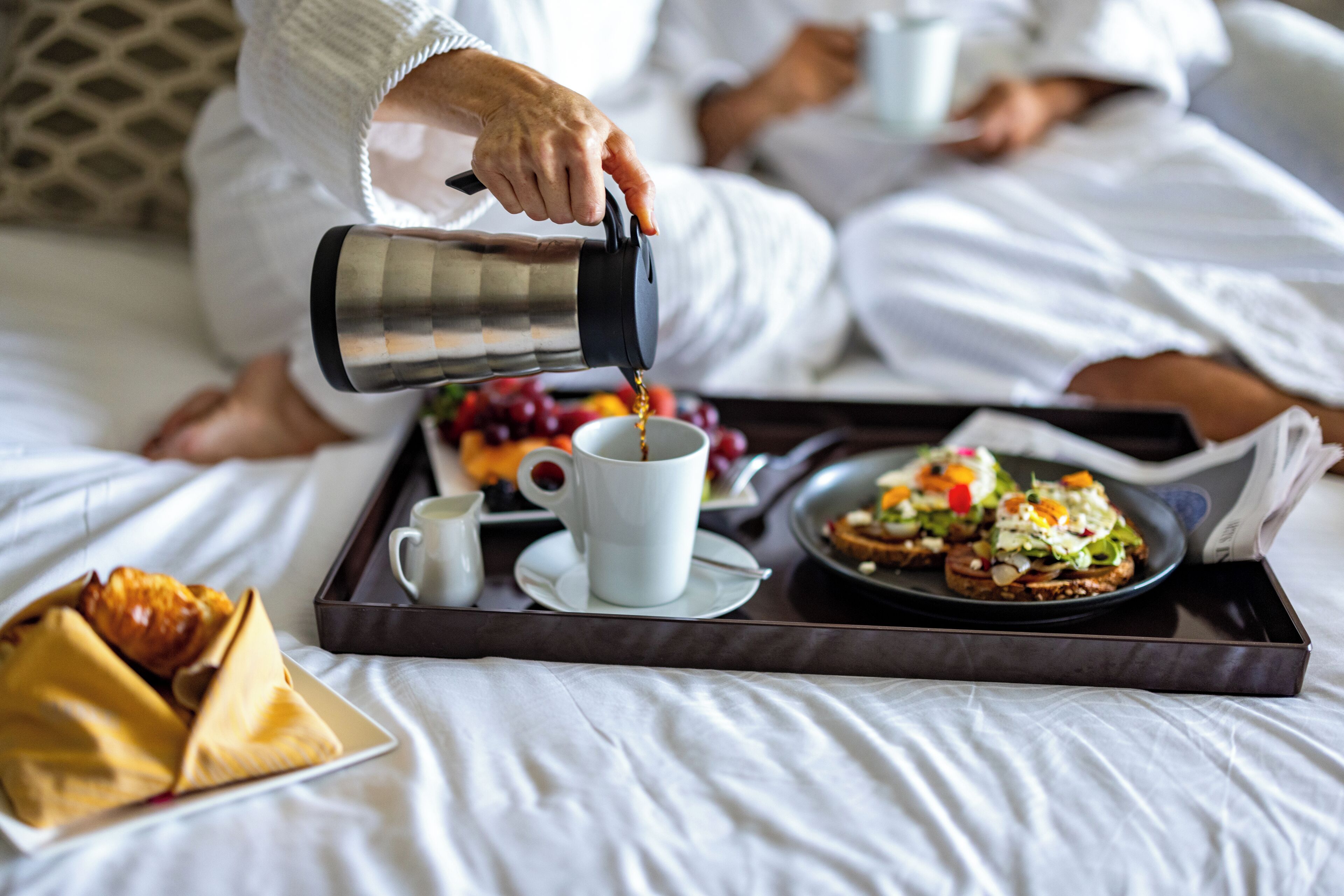 A tray with breakfast items including toast, fruit, and a cup of coffee on a bed.