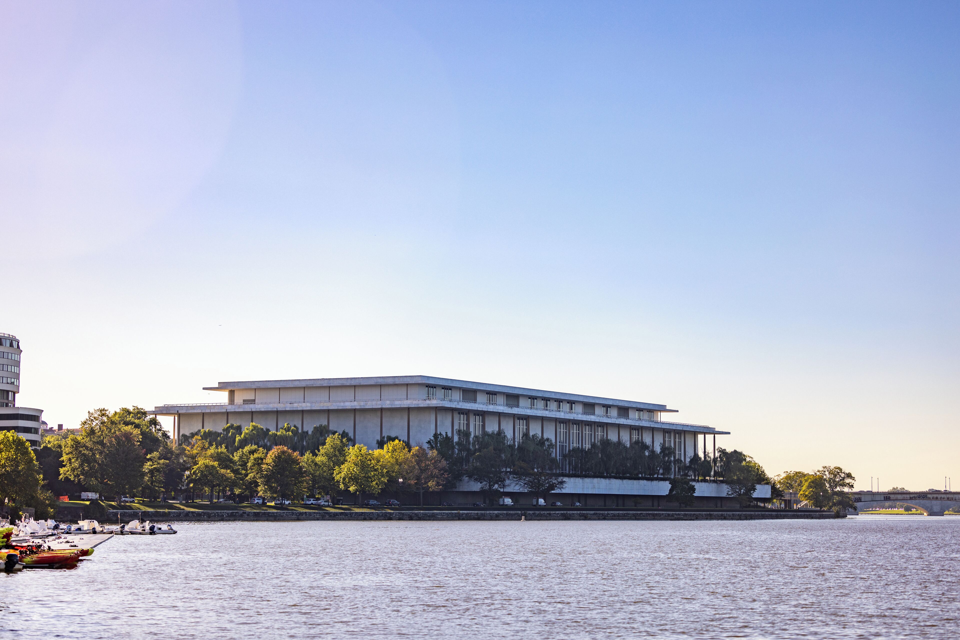 A modern building with a flat roof and large windows, located near a body of water with boats docked.