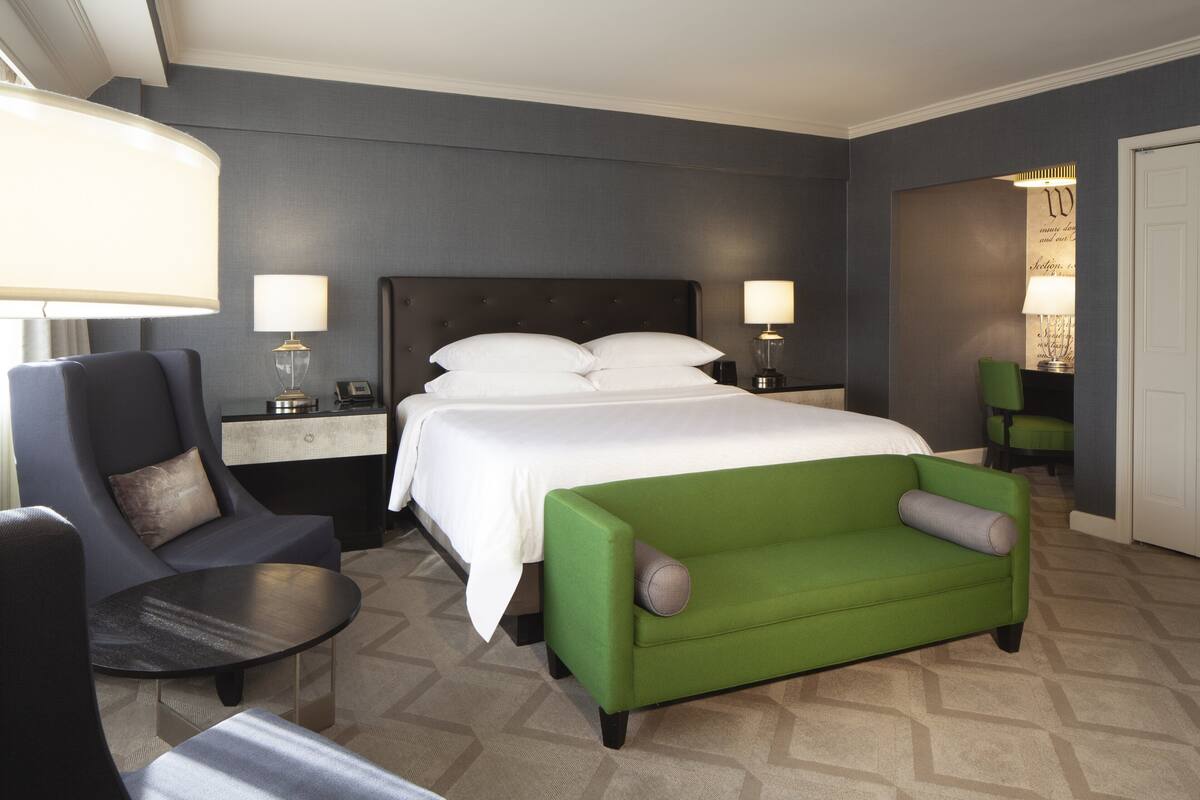 A hotel room with a bed, a green sofa, a round table, and two lamps.