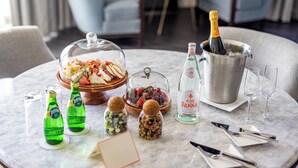 Una mesa dispuesta con una botella de champán, copas, una botella de agua, un frutero y una botella de refresco.