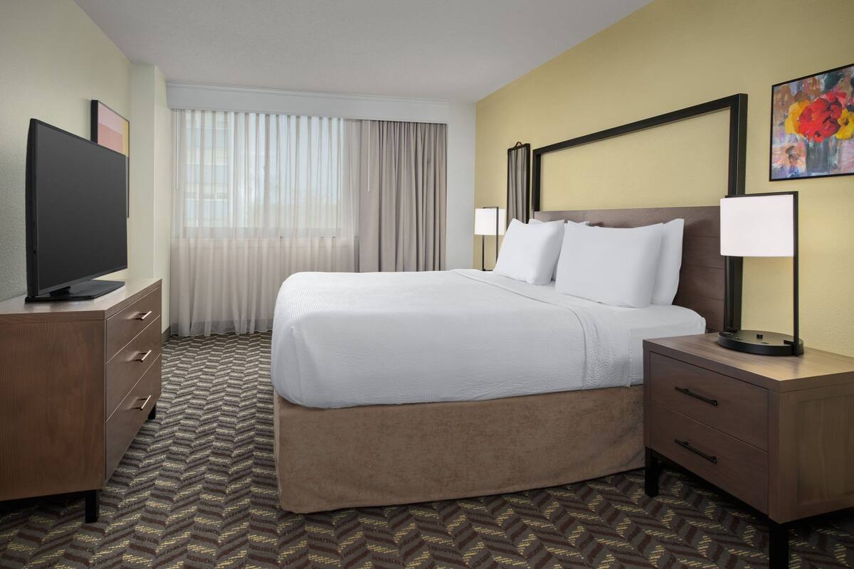 A hotel room with a large bed, a television, a desk, and a lamp.