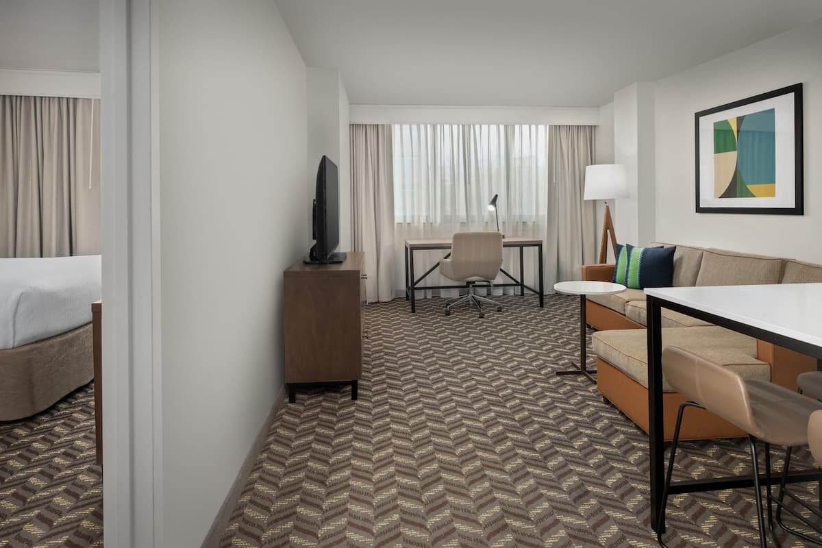 A hotel room with a bed, a desk, a chair, a sofa, and a television.