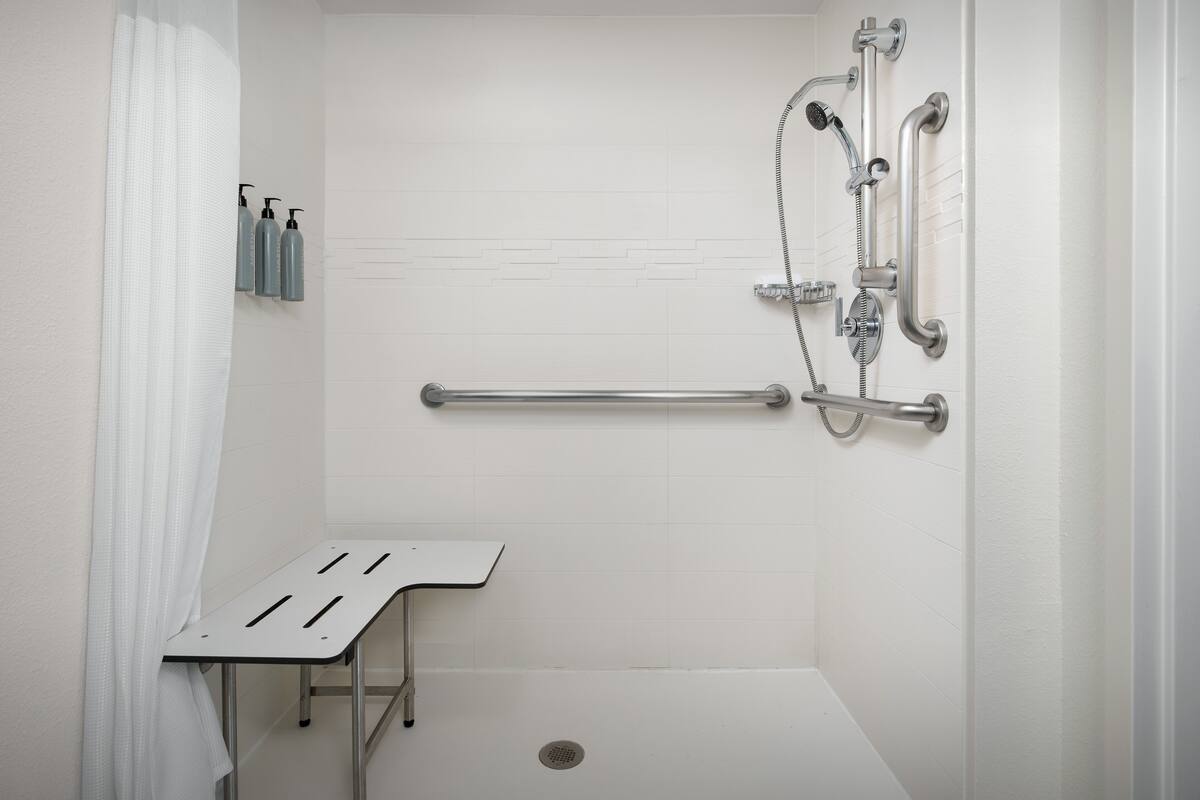 A modern bathroom with a walk-in shower, grab bars, and a bench.