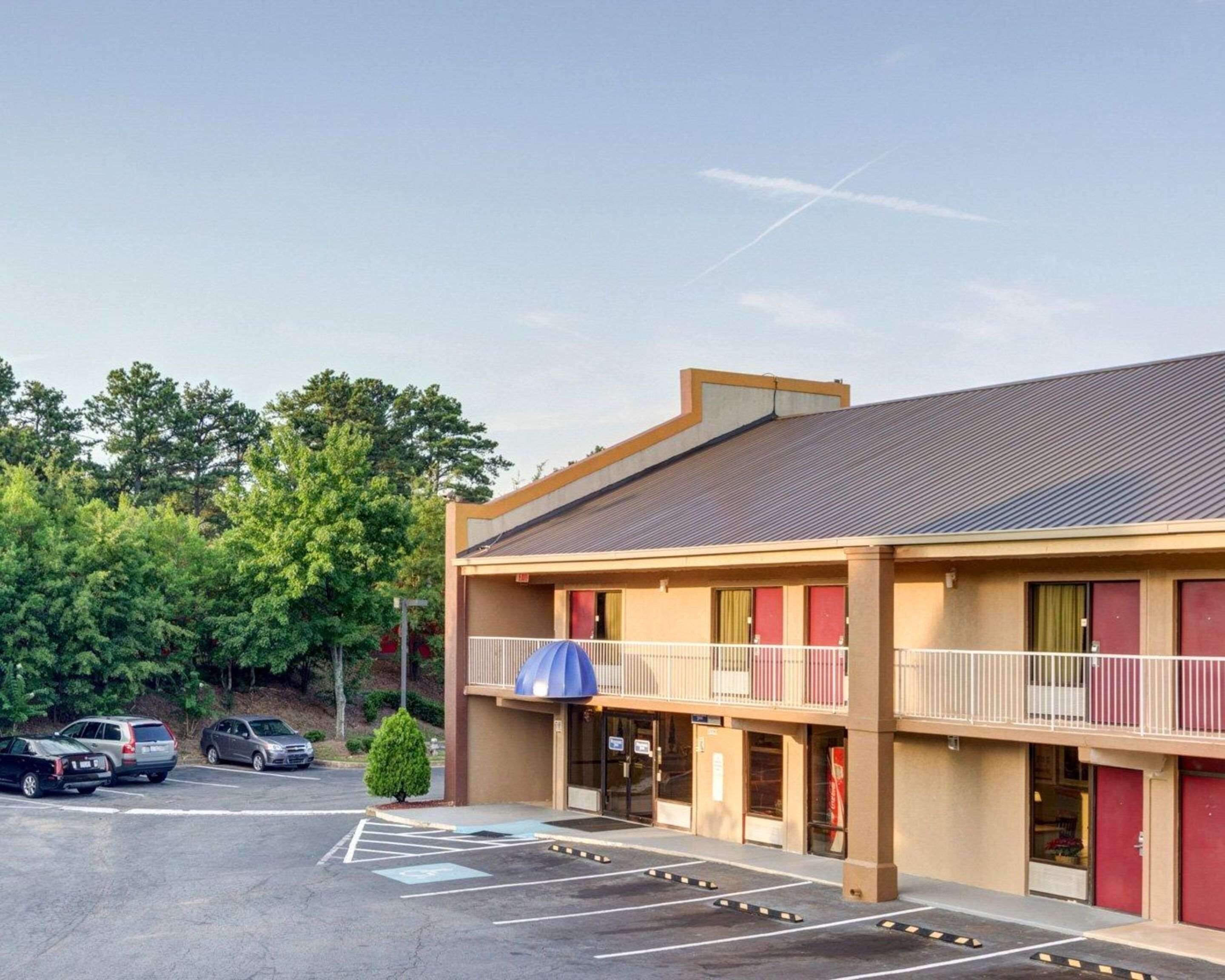 Un motel doté d’un parking, d’un espace extérieur abrité avec des sièges, et d’un bâtiment à deux étages avec un toit plat.