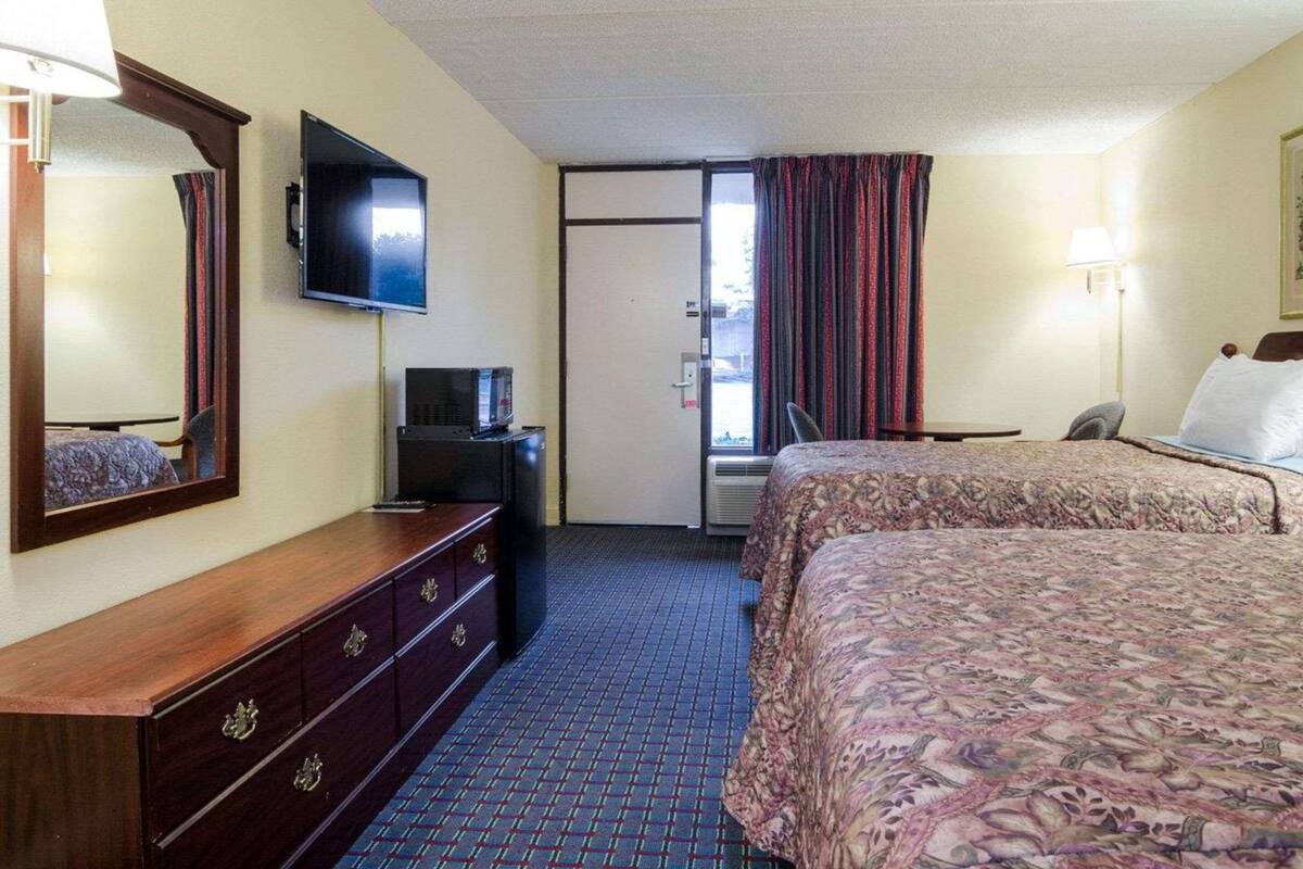 A hotel room with two beds, a TV, a dresser, and a door leading to a balcony.