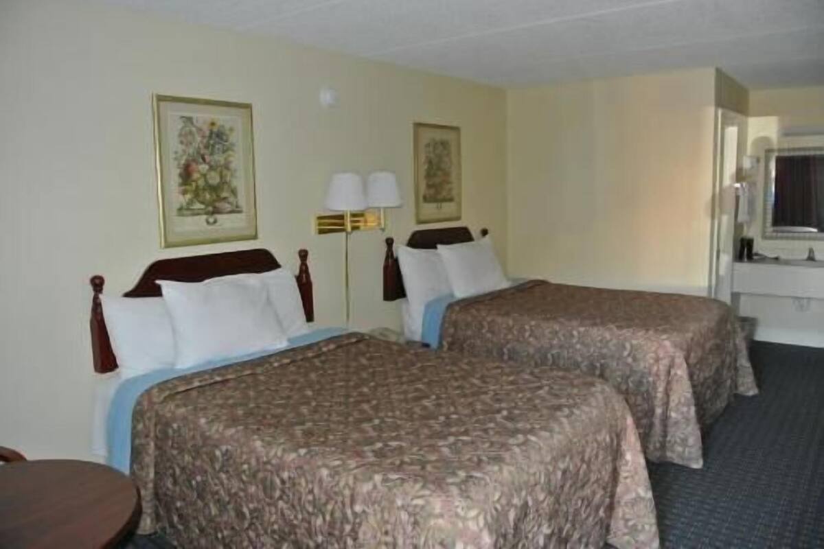 A hotel room with two beds, a desk, a chair, a window, and two wall-mounted lamps.