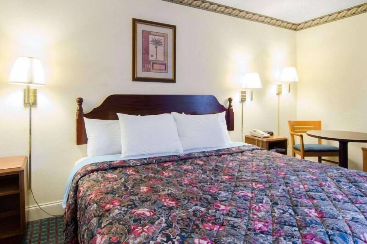 A hotel room with a bed, two bedside lamps, a small table, and a chair.