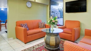 Ein Wohnzimmer mit zwei orangefarbenen Sofas, einem runden Couchtisch, einer Uhr und einem an der Wand befestigten Fernseher.