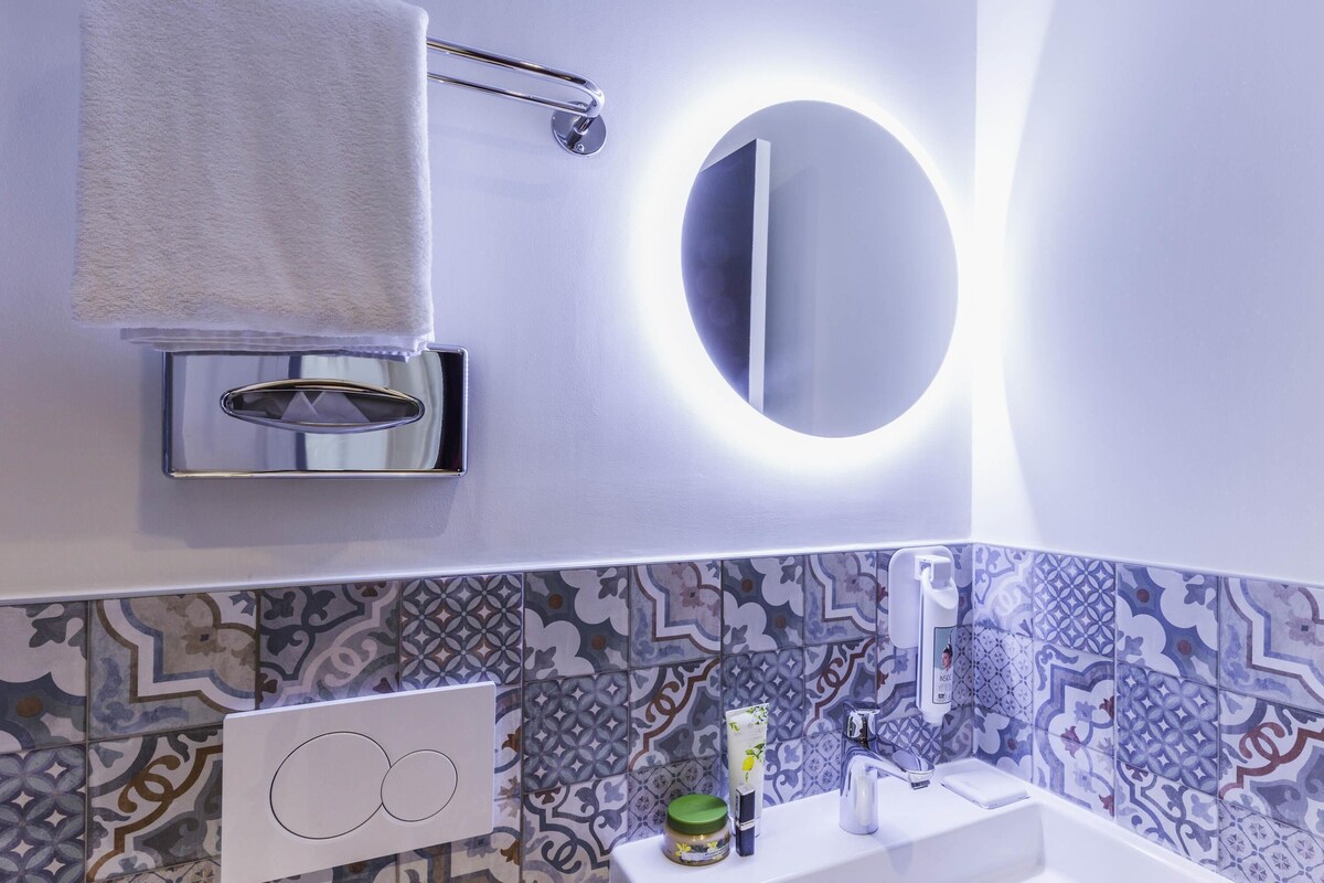 Een badkamer met een witte wastafel, een spiegel, een handdoekhouder en betegelde vloeren.