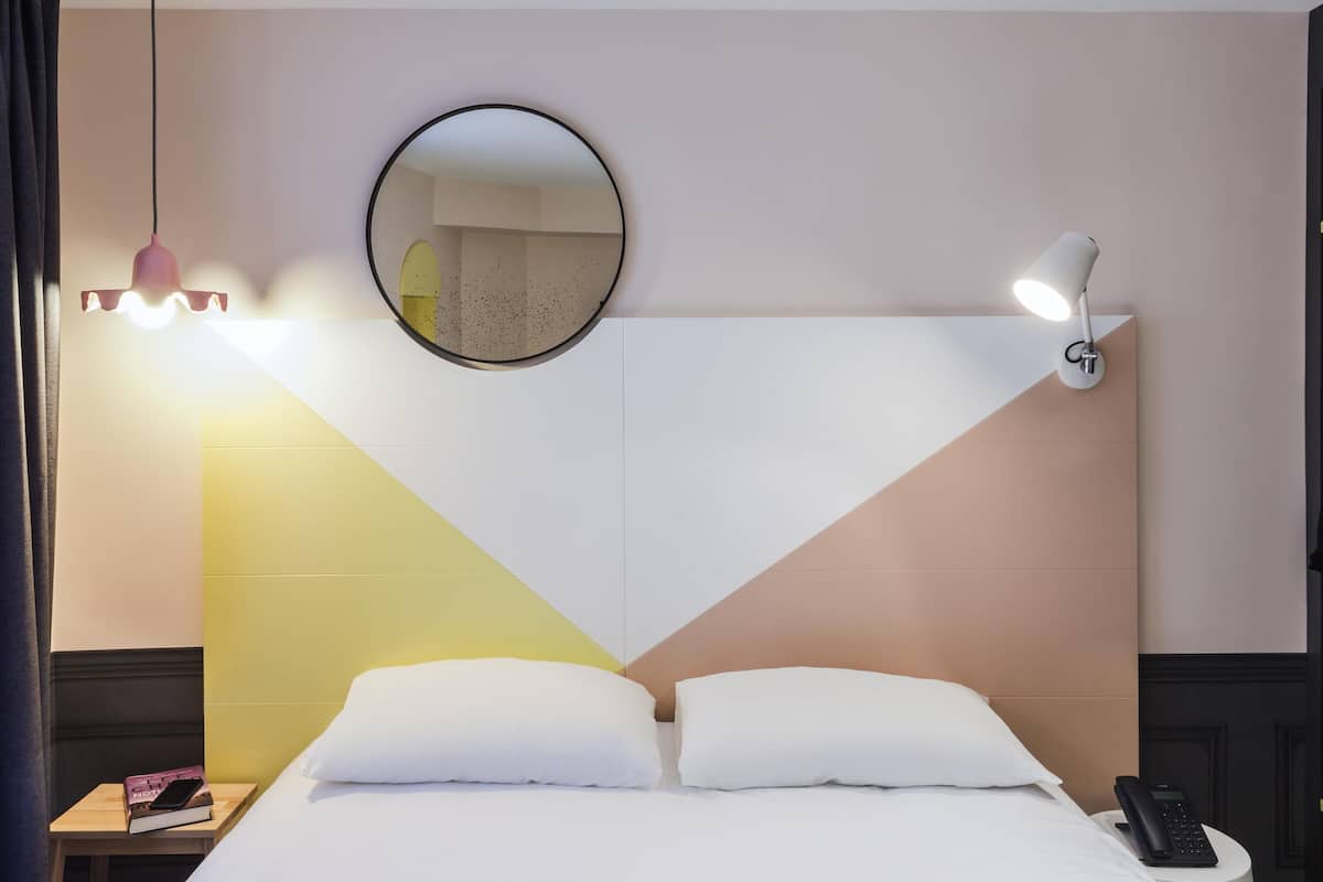 Een hotelkamer met een bed, een nachtkastje, een ronde spiegel, een wandlamp en een telefoon op het tafelblad.