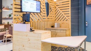 Un comptoir d’accueil avec un écran d’ordinateur, un mur en bois orné d’un motif en chevrons, une porte bleue et un sol à motifs.