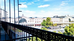 Un grand bâtiment historique, doté d’un dôme imposant et de fenêtres en arc de cercle, vu depuis un balcon orné d’une rambarde en métal.