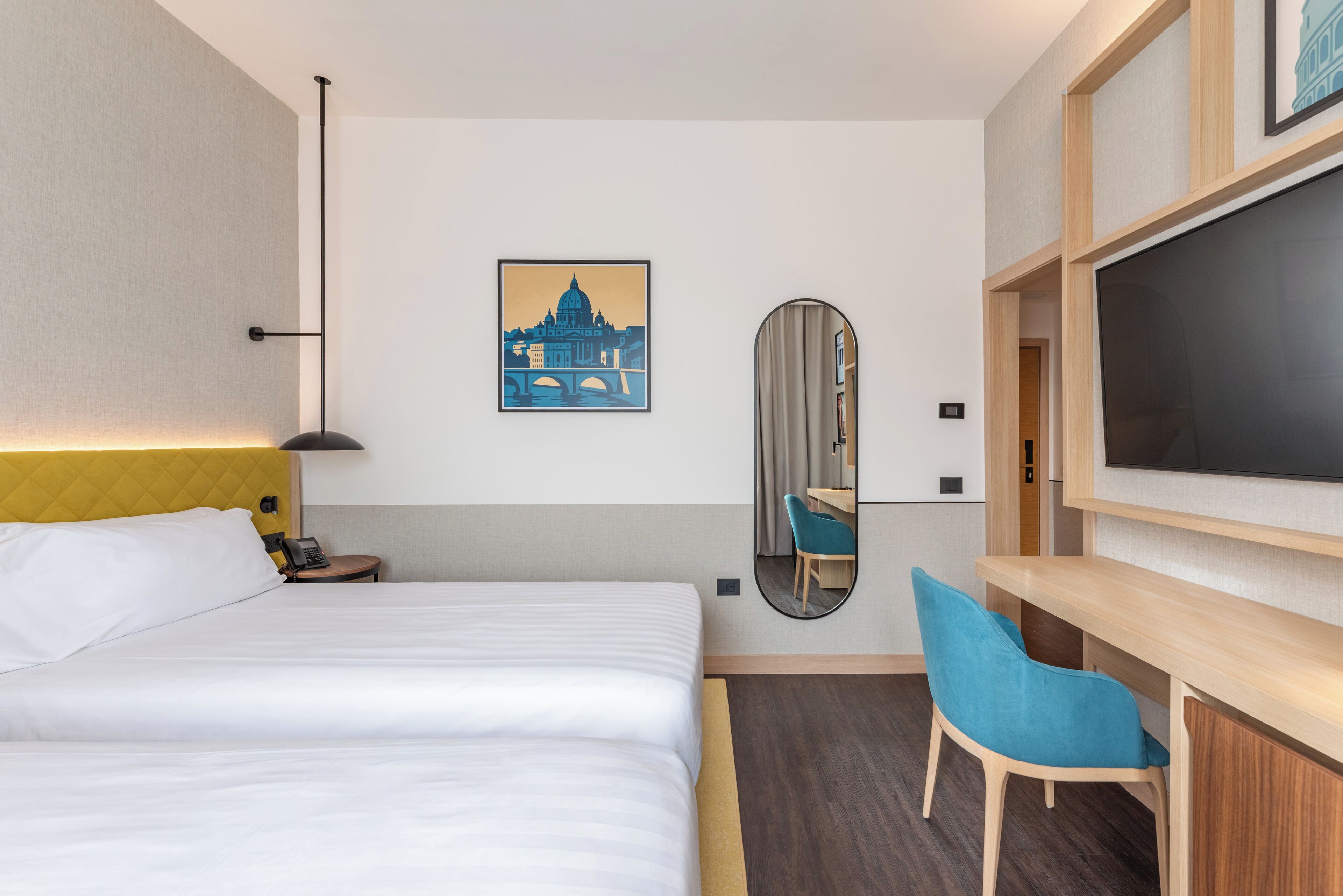 A hotel room with a bed, a desk, a chair, a TV, a mirror, and a painting of a bridge.