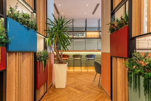 A hallway with wooden paneling, a potted plant, and a seating area with chairs and a table. - Hilton Garden Inn Rome Colosseum (Rome)