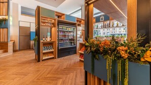 A modern retail space with wooden shelving, refrigerated display cases, and a view of the city through large windows. - Hilton Garden Inn Rome Colosseum (Rome)