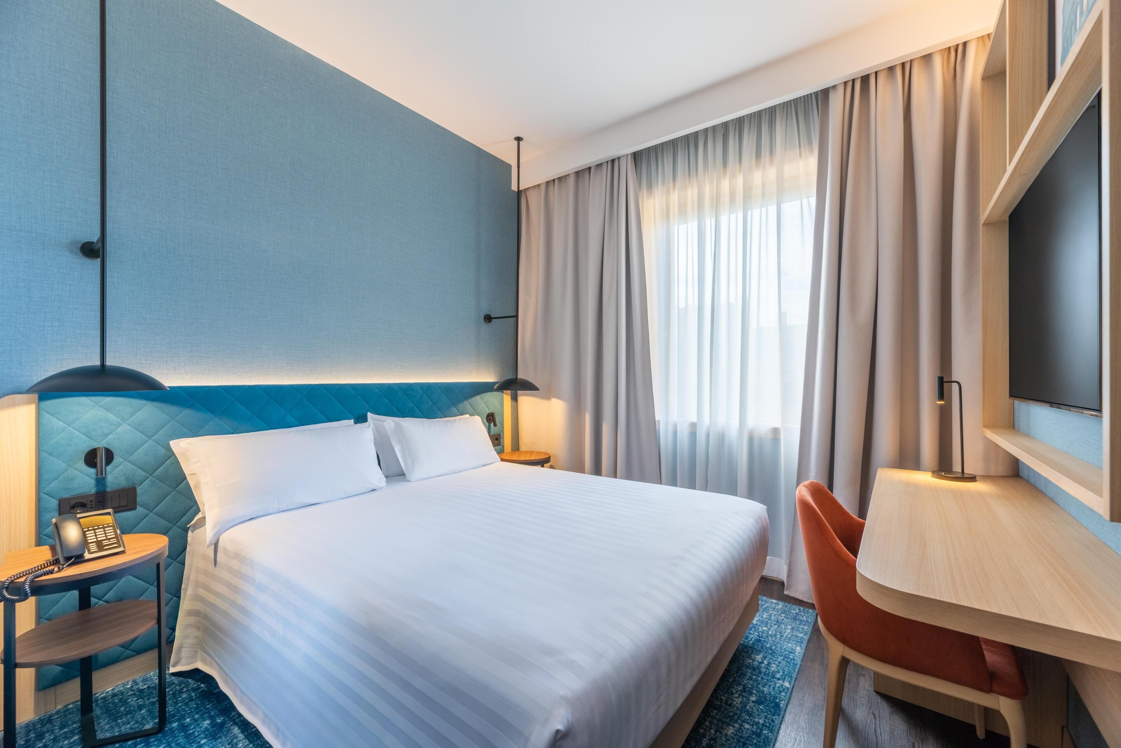 Una habitación de hotel con cama, escritorio, silla, teléfono y televisor.