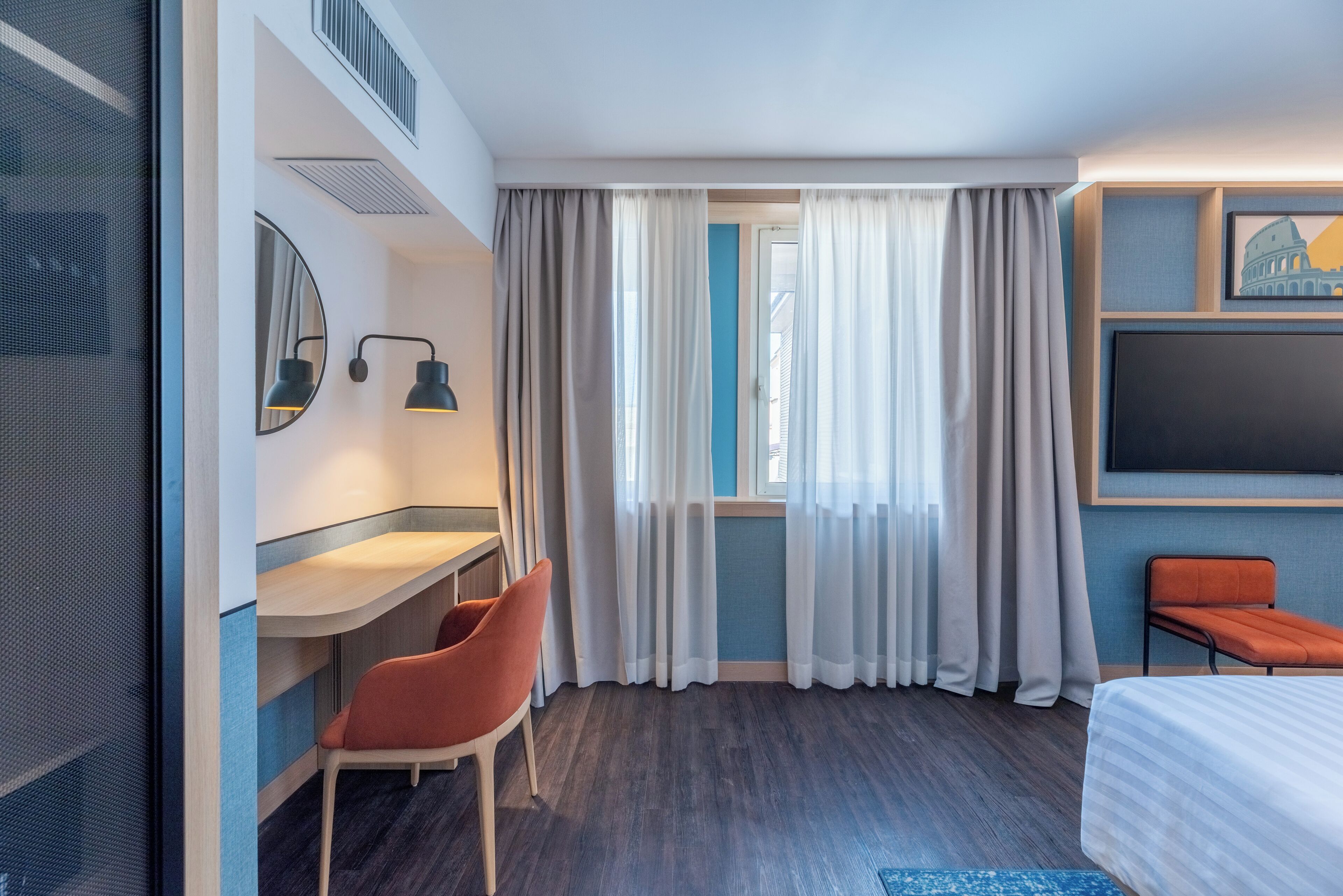 A hotel room with a bed, a desk with a chair, a TV, and curtains.