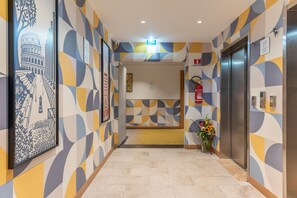 A hallway with patterned walls, an elevator, and a fire extinguisher. - Hilton Garden Inn Rome Colosseum (Rome)