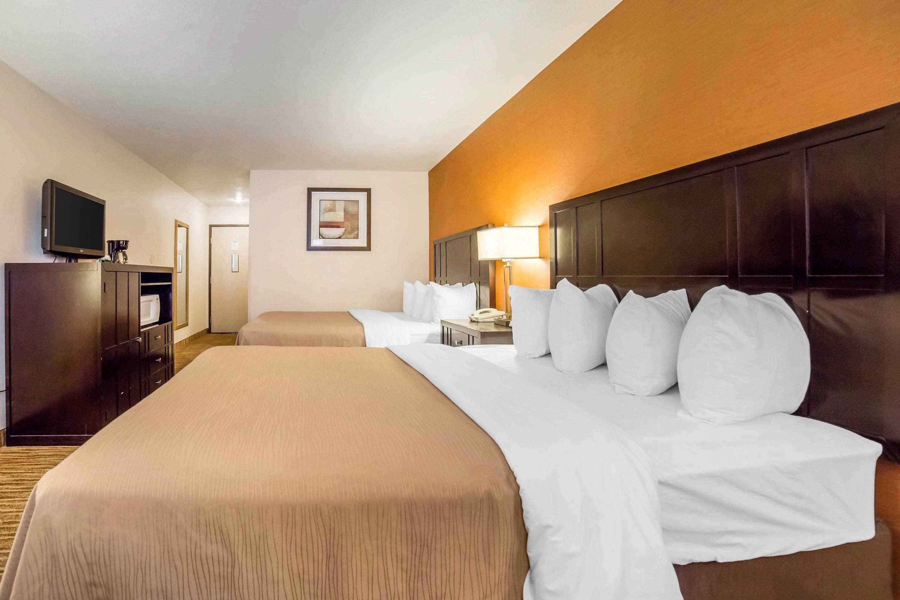 A hotel room with a large bed, a desk with a lamp, a television, and a framed picture on the wall.