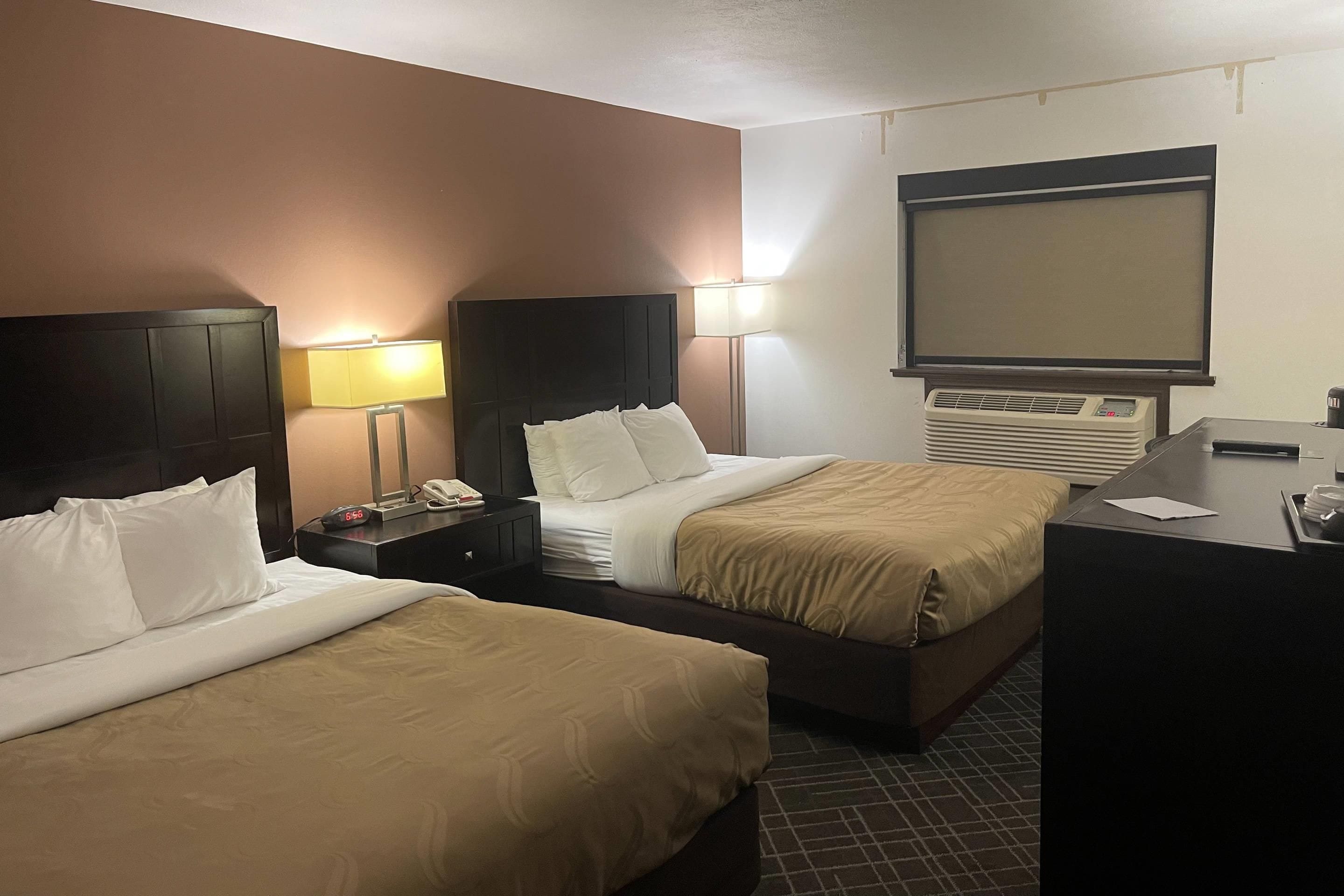 A hotel room with two beds, a desk, a chair, a TV, and a window.