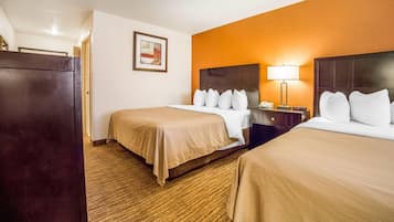 Habitación de hotel con dos camas, una mesita de noche, una lámpara, un cuadro enmarcado en la pared y piso alfombrado.