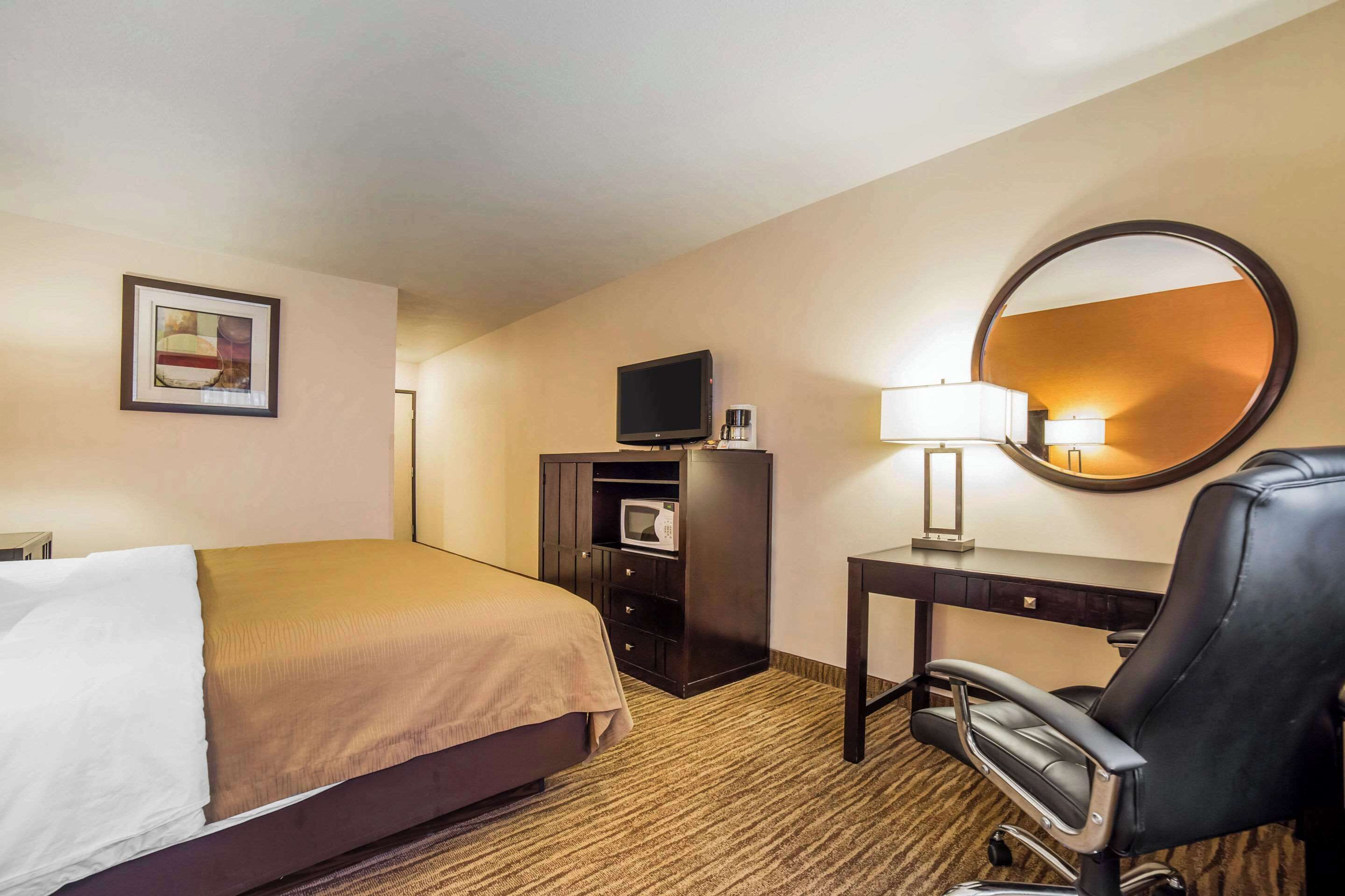 A hotel room with a bed, a desk with a chair, a television, a microwave, and a mirror.