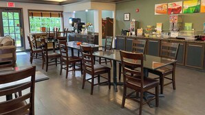 A restaurant with wooden tables and chairs, a kitchen area, and a menu board on the wall.
