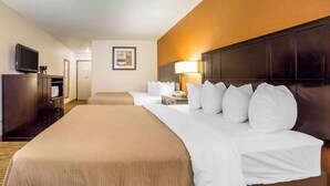 A hotel room with a large bed, a television, a desk with a lamp, and a framed picture on the wall.
