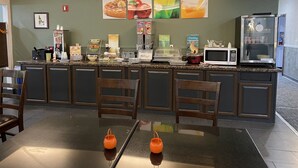 Una barra de desayuno con asientos, microondas, refrigerador y diversas opciones de comida.