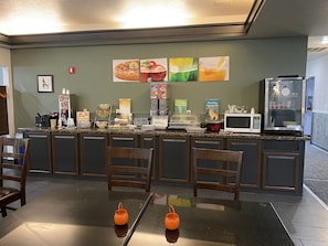 A breakfast bar with seating, a microwave, a refrigerator, and various food items.