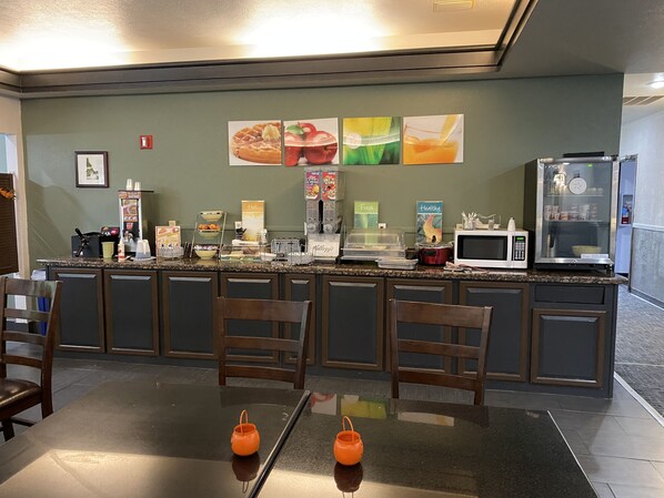 Una barra de desayuno con asientos, microondas, refrigerador y diversas opciones de comida.
