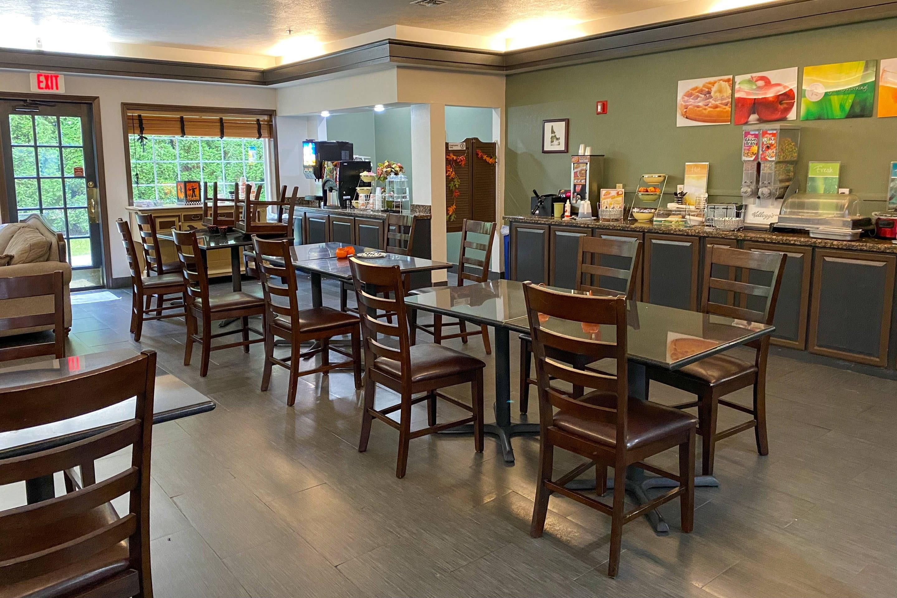 A dining area with wooden tables and chairs, a kitchen counter with food items, and an exit sign.