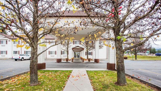 A building with a covered entrance, a sidewalk leading to it, and trees with autumn leaves.